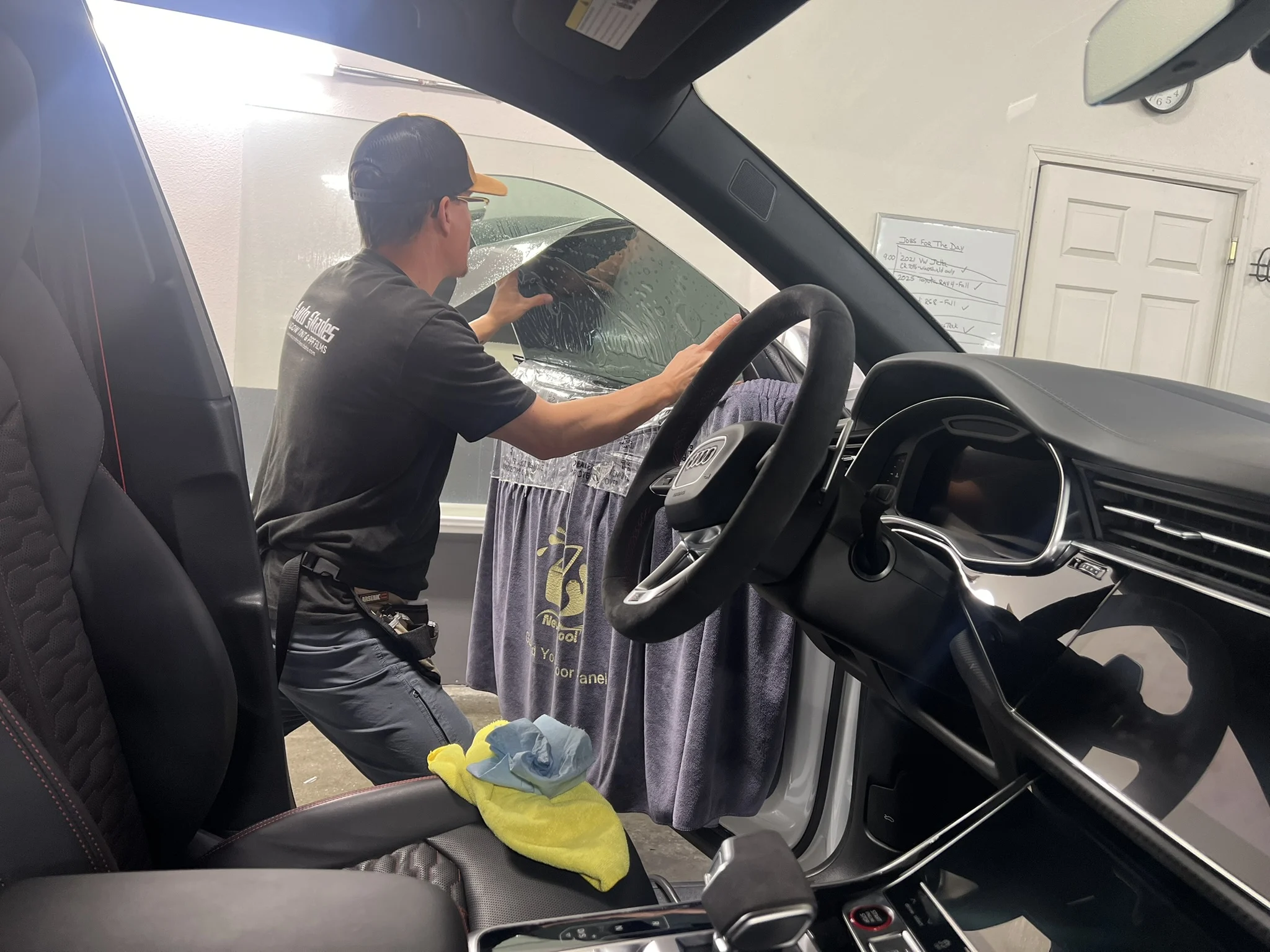 Technician from Auto Shades installs window tint on a front door window of an Audi, viewed from the interior with tools and towels protecting the door panel.