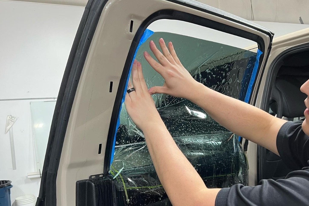 A professional installer smooths out freshly applied window film on a vehicle door using their hands, with soapy water and tape aiding in precise alignment—demonstrating the expert process behind What Window Tinting Really Is.