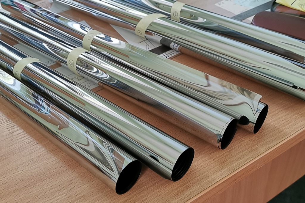 Rolls of reflective metallic window film laid out on a wooden table, showcasing one of the material types used in car tinting and illustrating options in What Window Tinting Really Is.