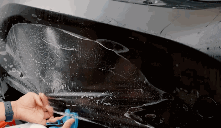 Technician applying and adjusting paint protection film on a car’s rear quarter panel with a wet installation method.