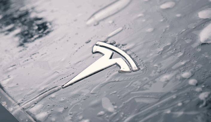 Close-up of a Tesla logo on a wet car hood during the application of paint protection film.